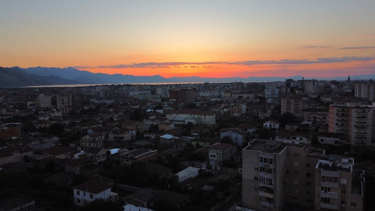 a sunset over a city with mountains in the background